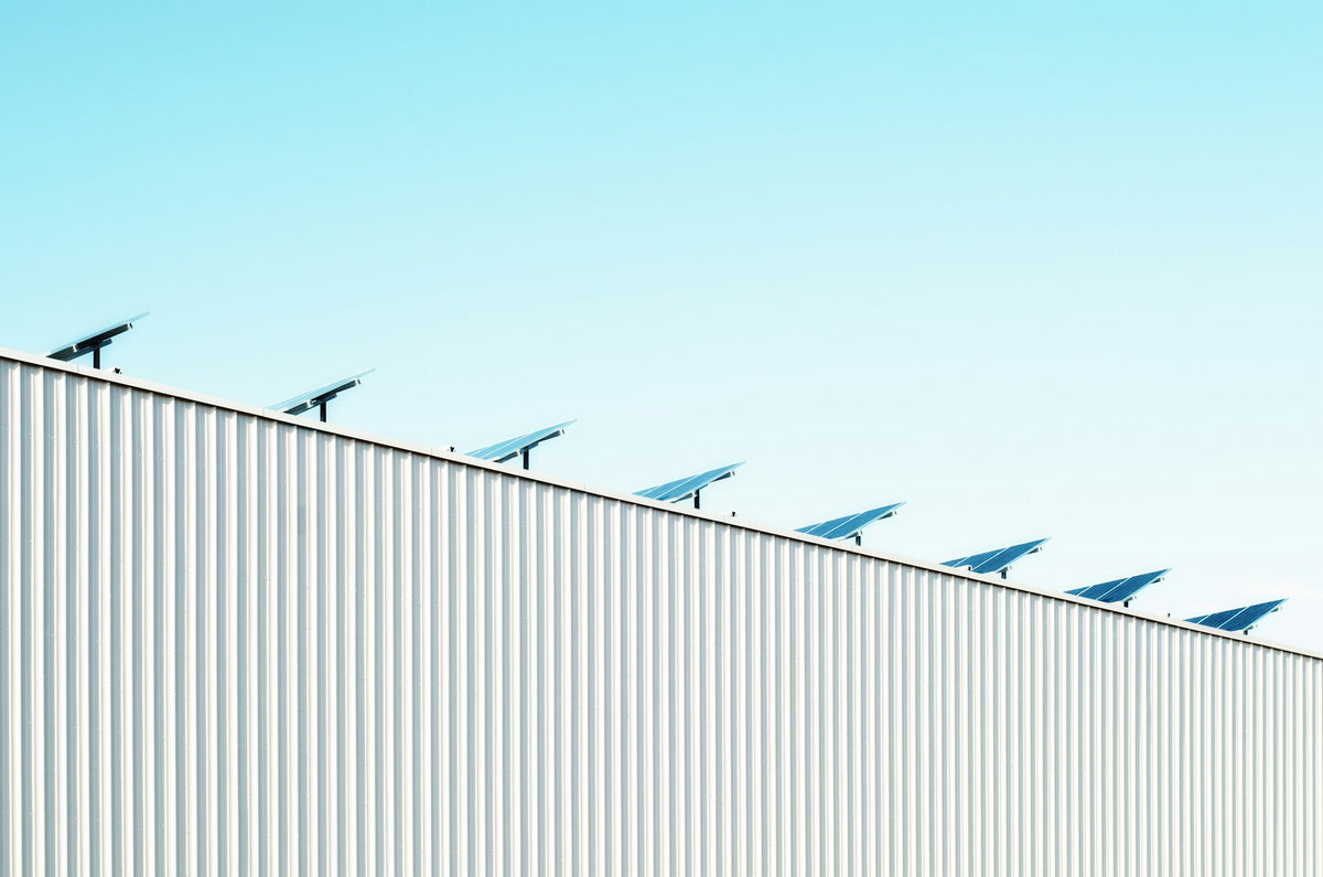 Solar panels installed along the roofline of a white corrugated metal building under a clear light blue sky.