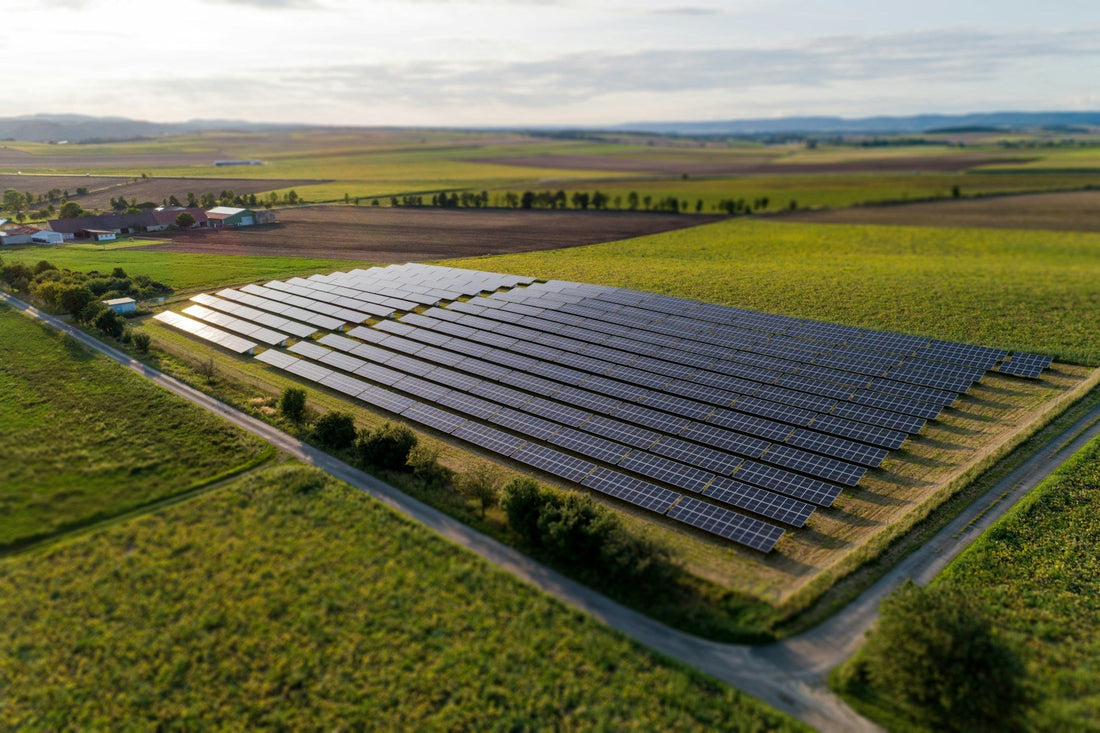 Aerial view of a ground-mounted solar farm with rows of solar panels surrounded by green farmland.