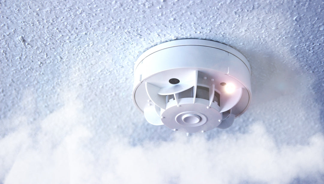 Ceiling-mounted smoke detector with red indicator light activated, surrounded by smoke.