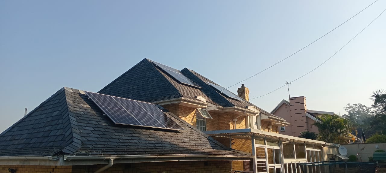 Tiled residential rooftop with solar panel arrays installed across multiple sections, under a clear blue sky.