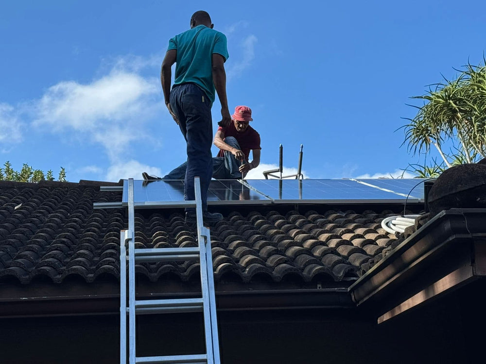 Two people installing solar panels on a roof with a clear blue sky.